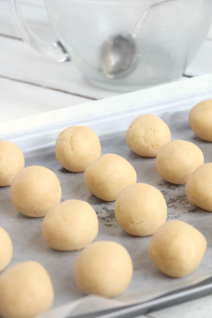 Cake pops lined up on a baking sheet lined with wax paper.