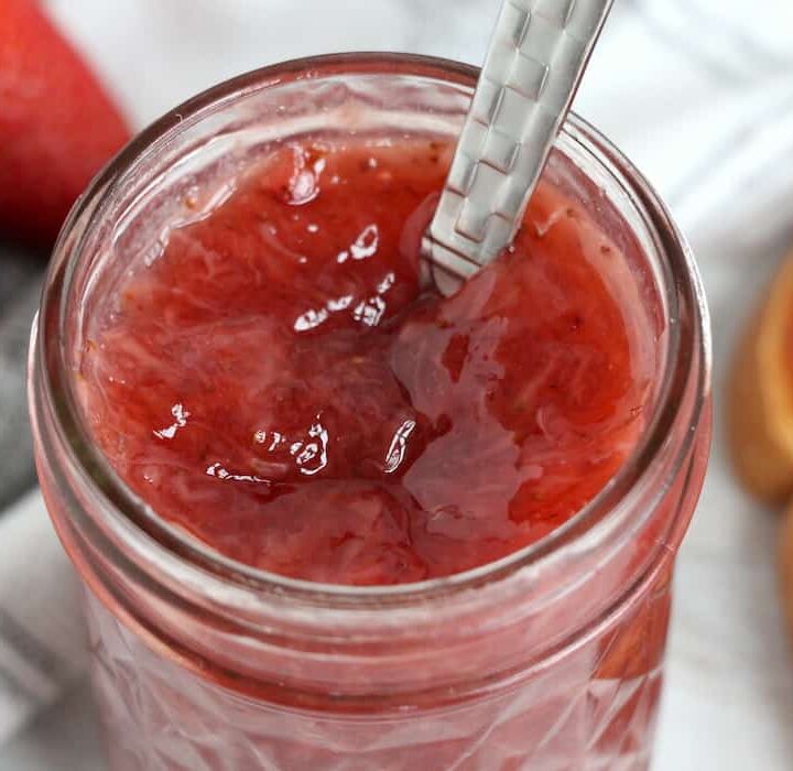 Instant Pot Strawberry Jam in a jar with a spoon in it. Jam shown on toast with strawberries.