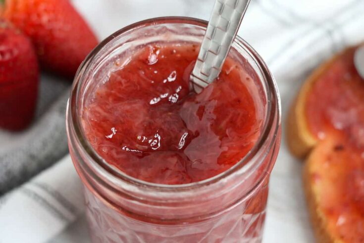 Instant Pot Strawberry Jam in a jar with a spoon in it. Jam shown on toast with strawberries.