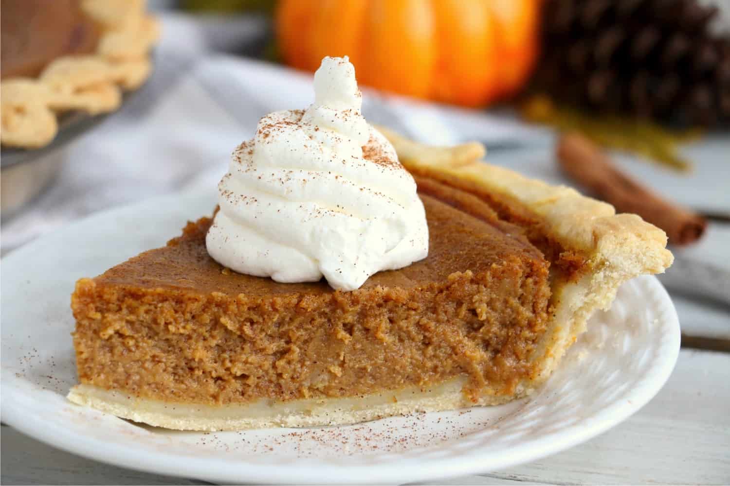 A piece of pumpkin pie on a white plate, surrounded by fall decorations.