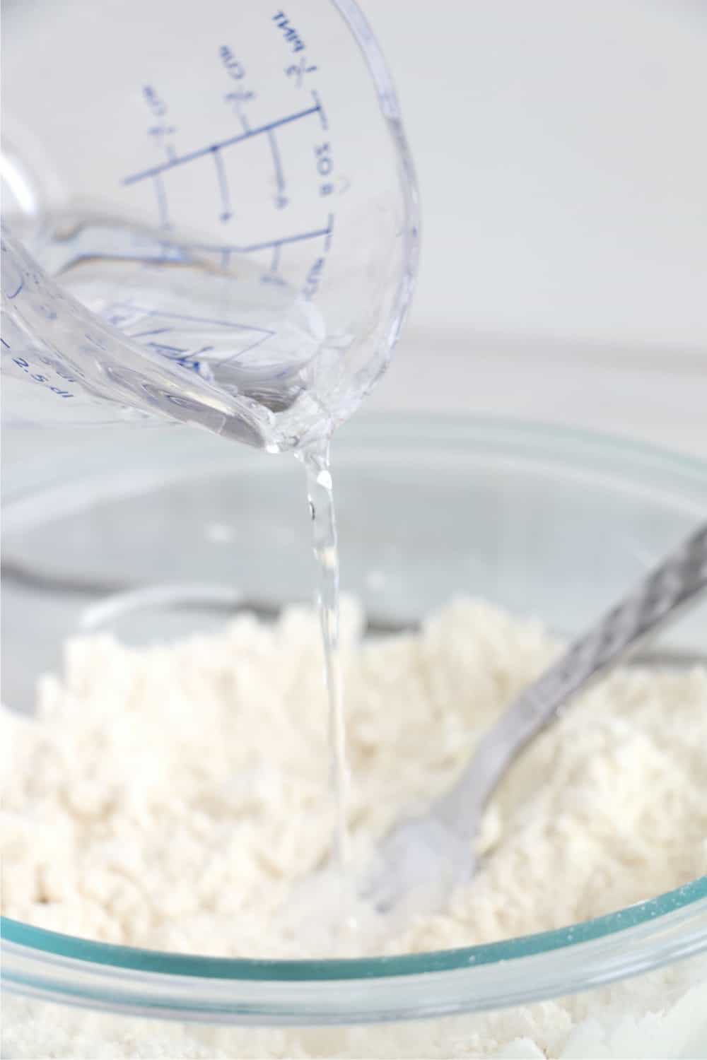 Pouring water into flour mixture while making pie crust.