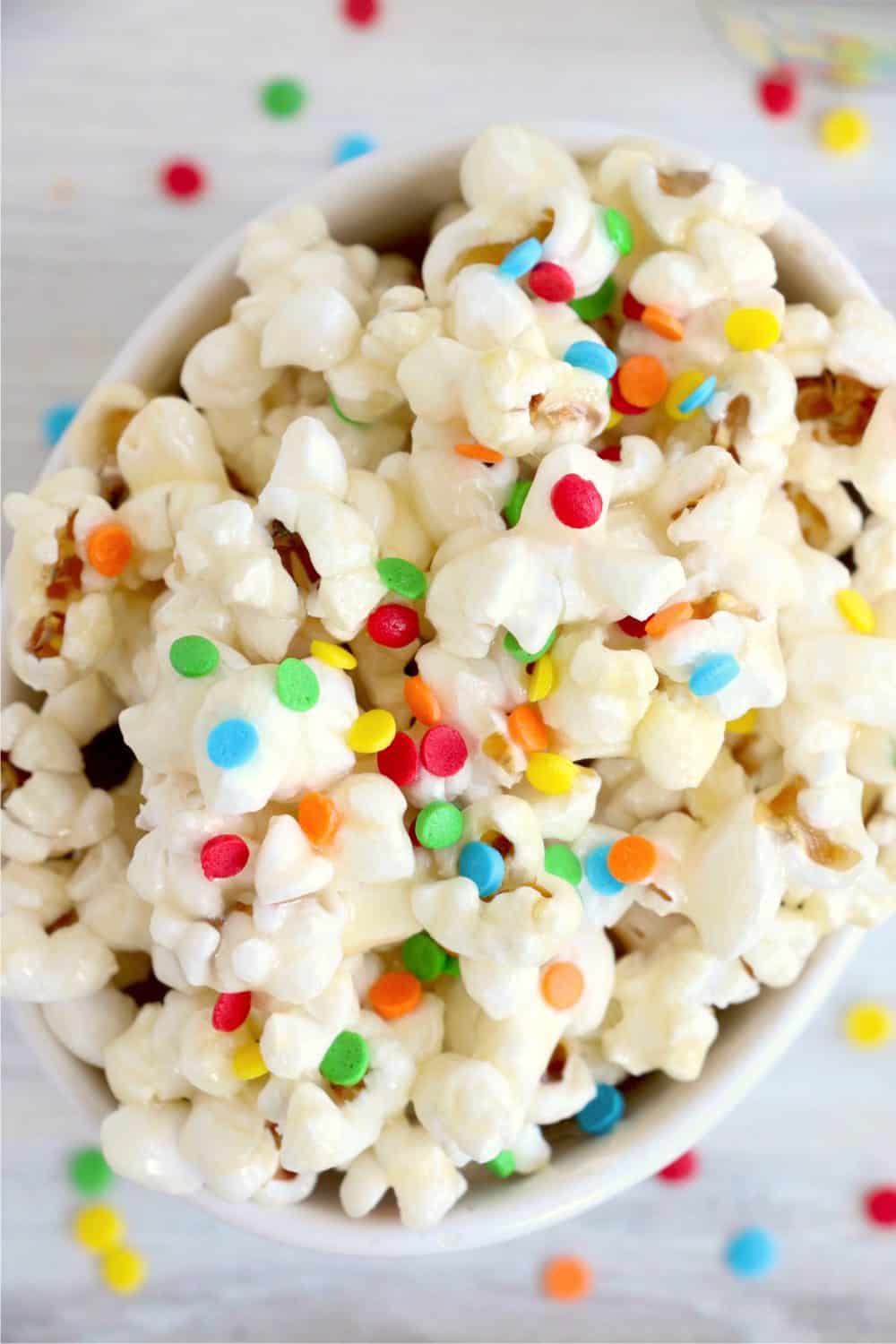 Vanilla glazed popcorn with sprinkles in a white bowl.