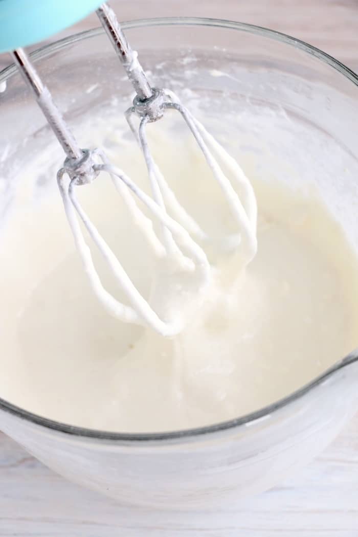 Cream cheese layer in a mixing bowl with a hand mixer.