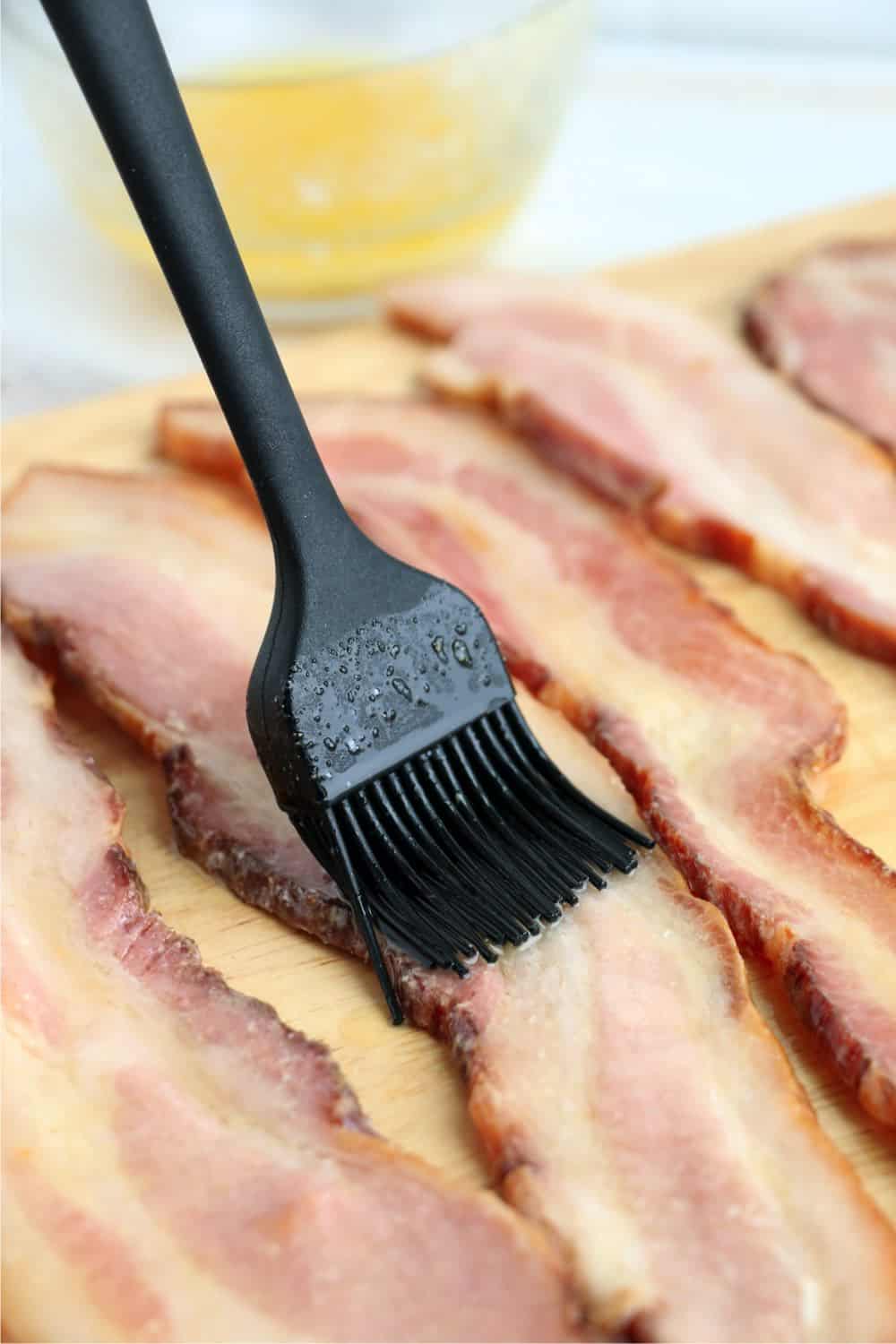 Melted butter, salt and garlic powder mixture being brushed onto strips of bacon