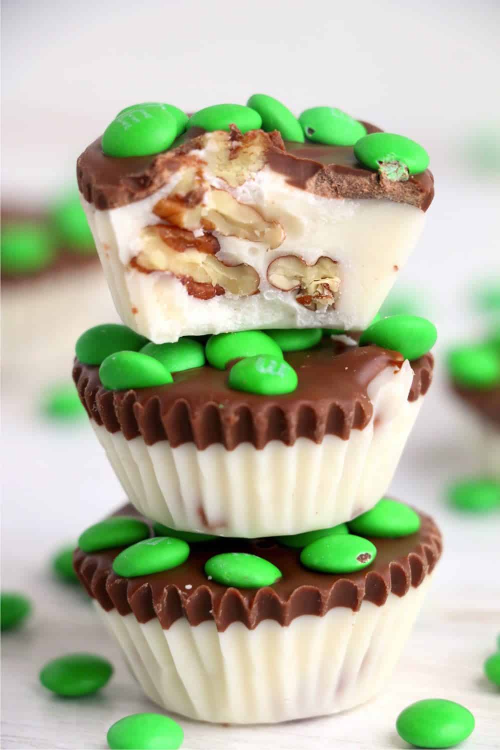 Chocolate Pecan Clusters piled up with green M&Ms candies. A bite is taken out of the chocolate candy on top.