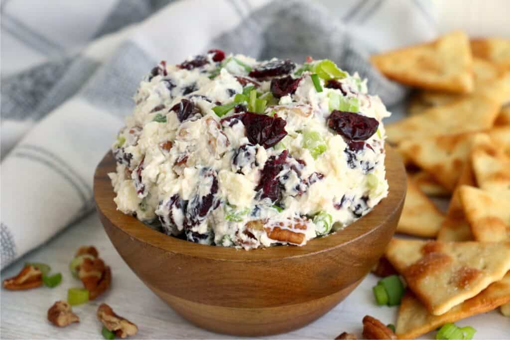 A heaping bowl of cheese ball dip with crackers scattered behind