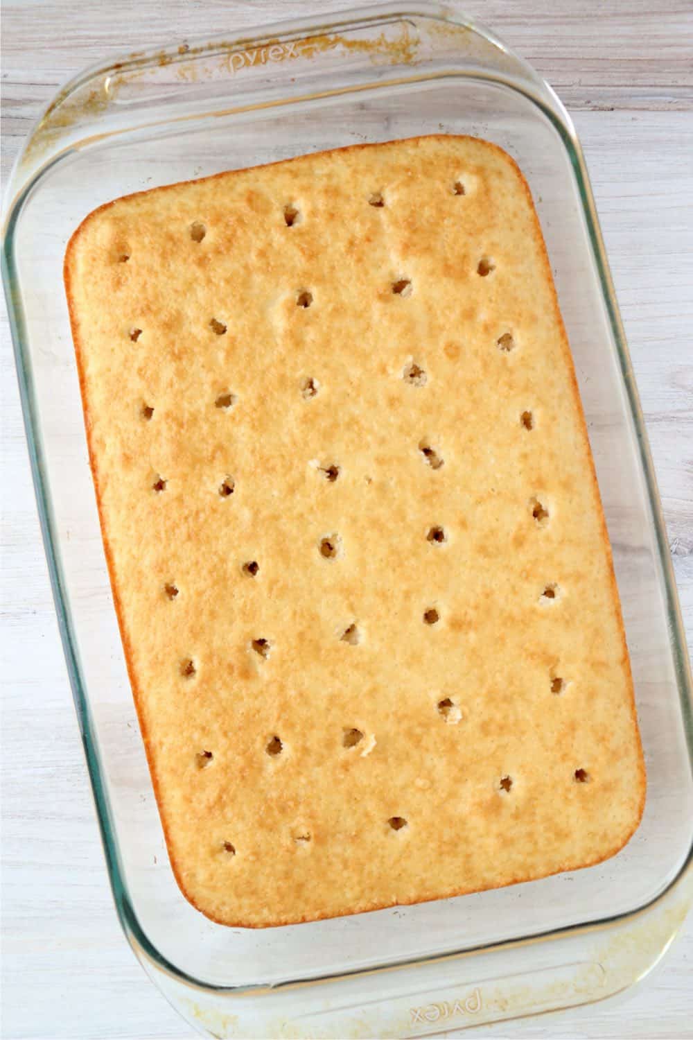 A baked cake with holes poked in it, ready for jello to be poured overtop.