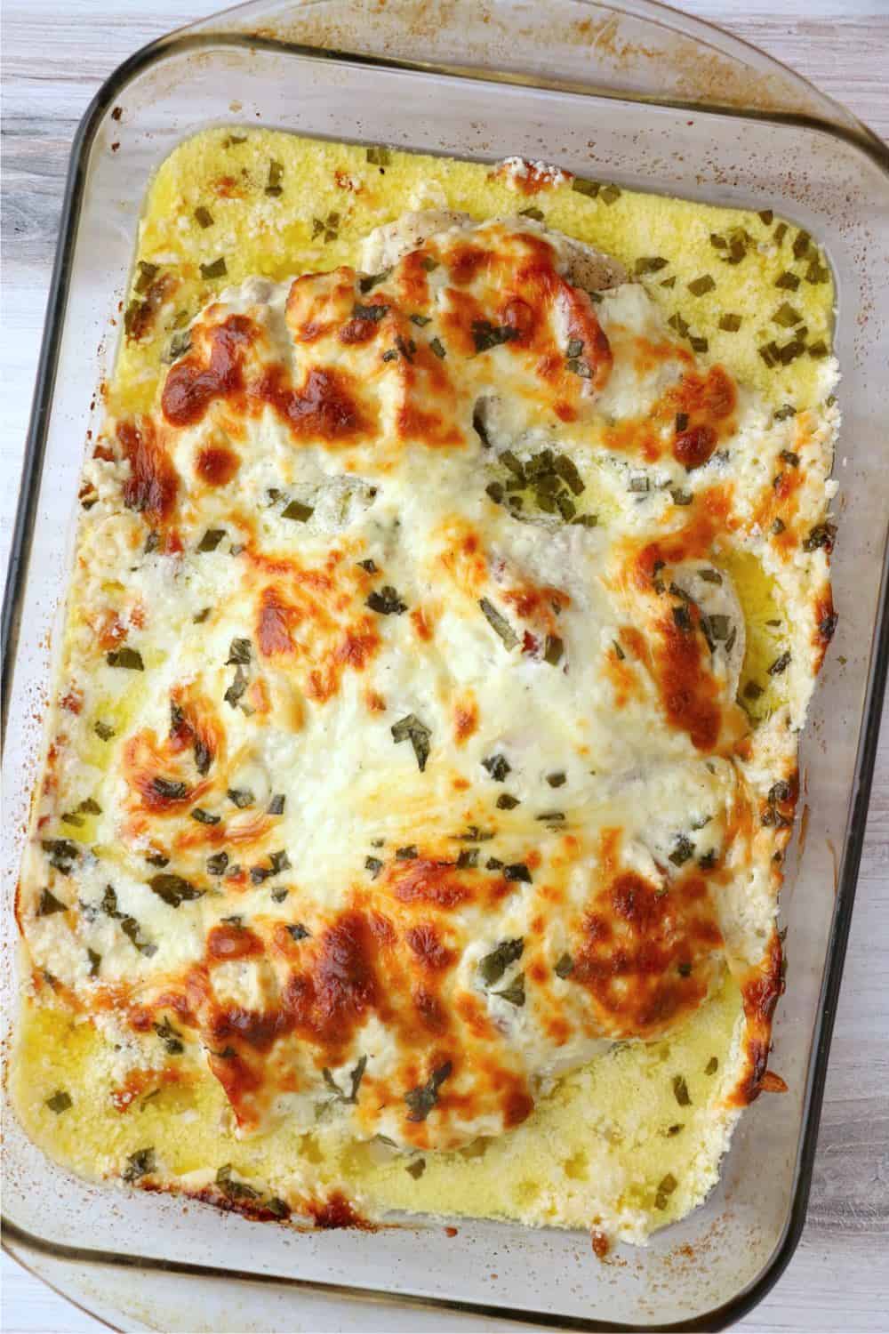 A baking dish filled with stuffed chicken breasts, covered in a cheesy sauce.