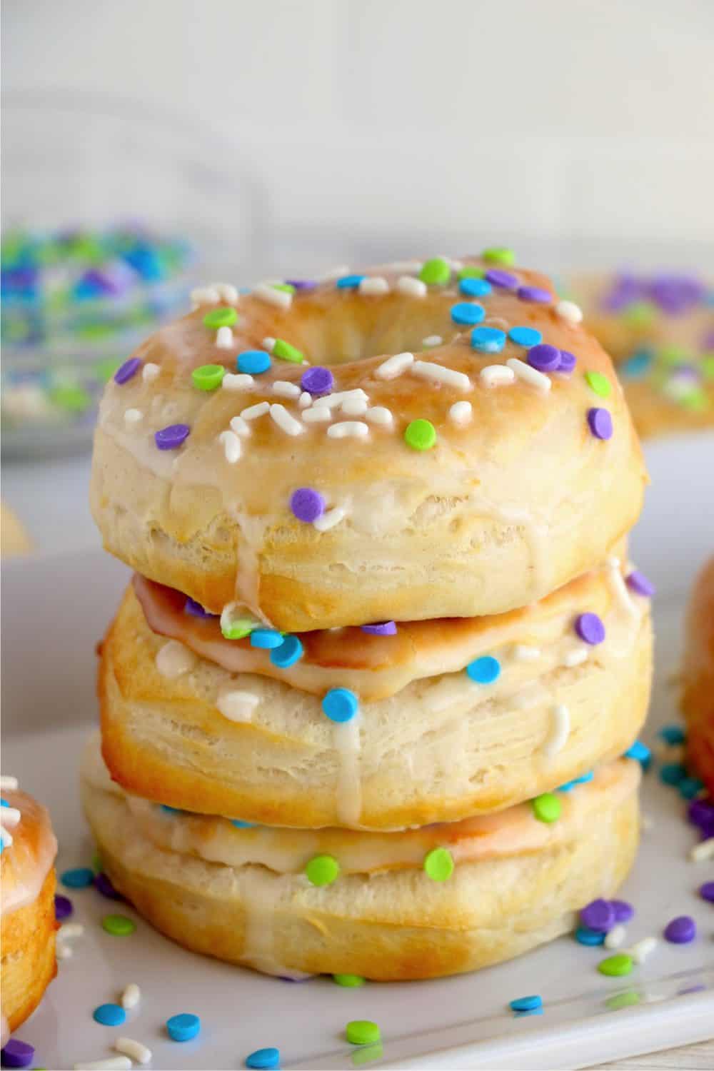 Air fryer donuts from biscuits with sprinkles and icing stacked up on top of each other