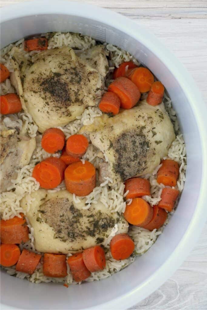 An overhead shot of chicken thighs with rice in an instant pot. There are also chopped carrots sprinkled throughout