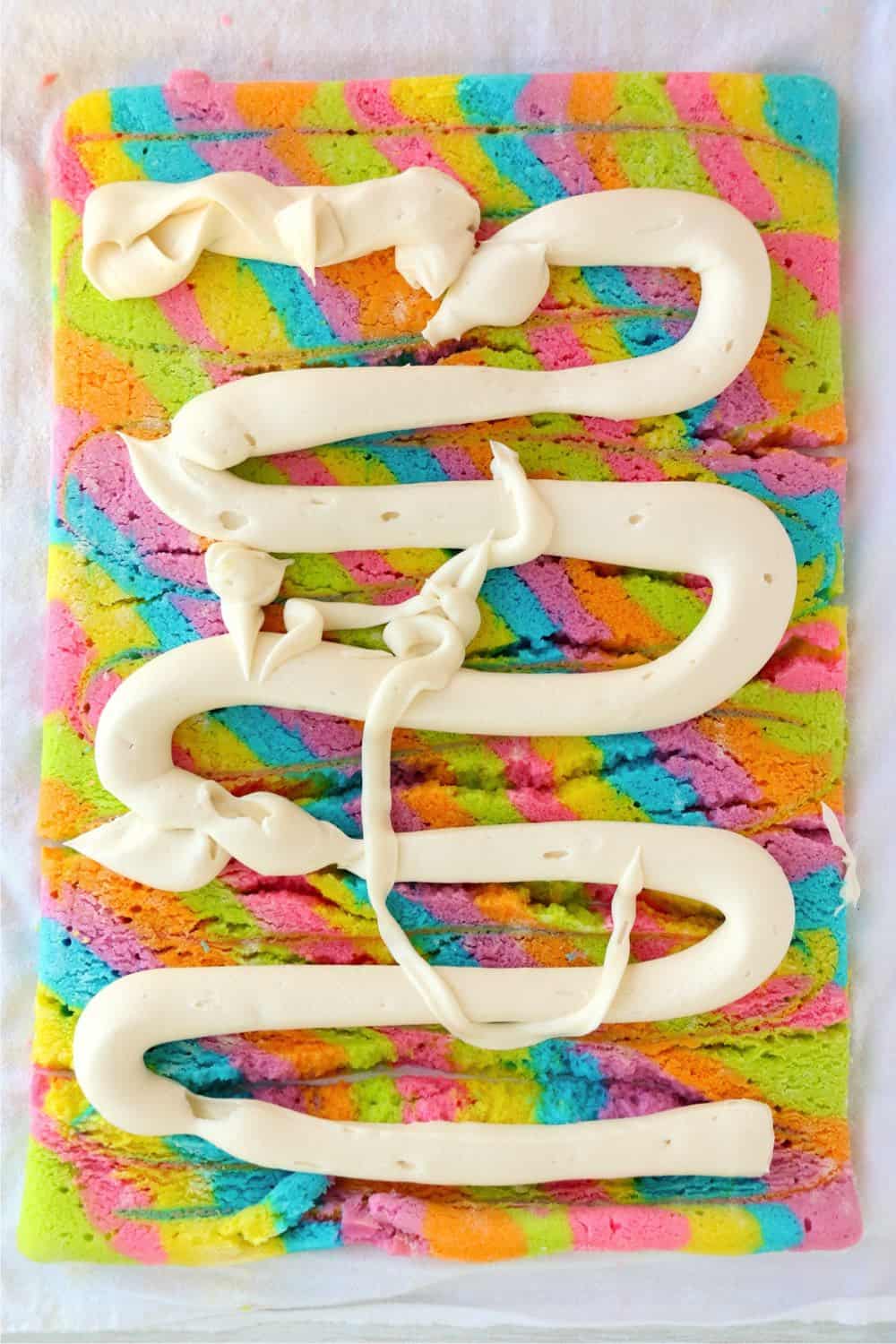 An overhead shot of tie dye vanilla roll cake with icing prepared to be spread