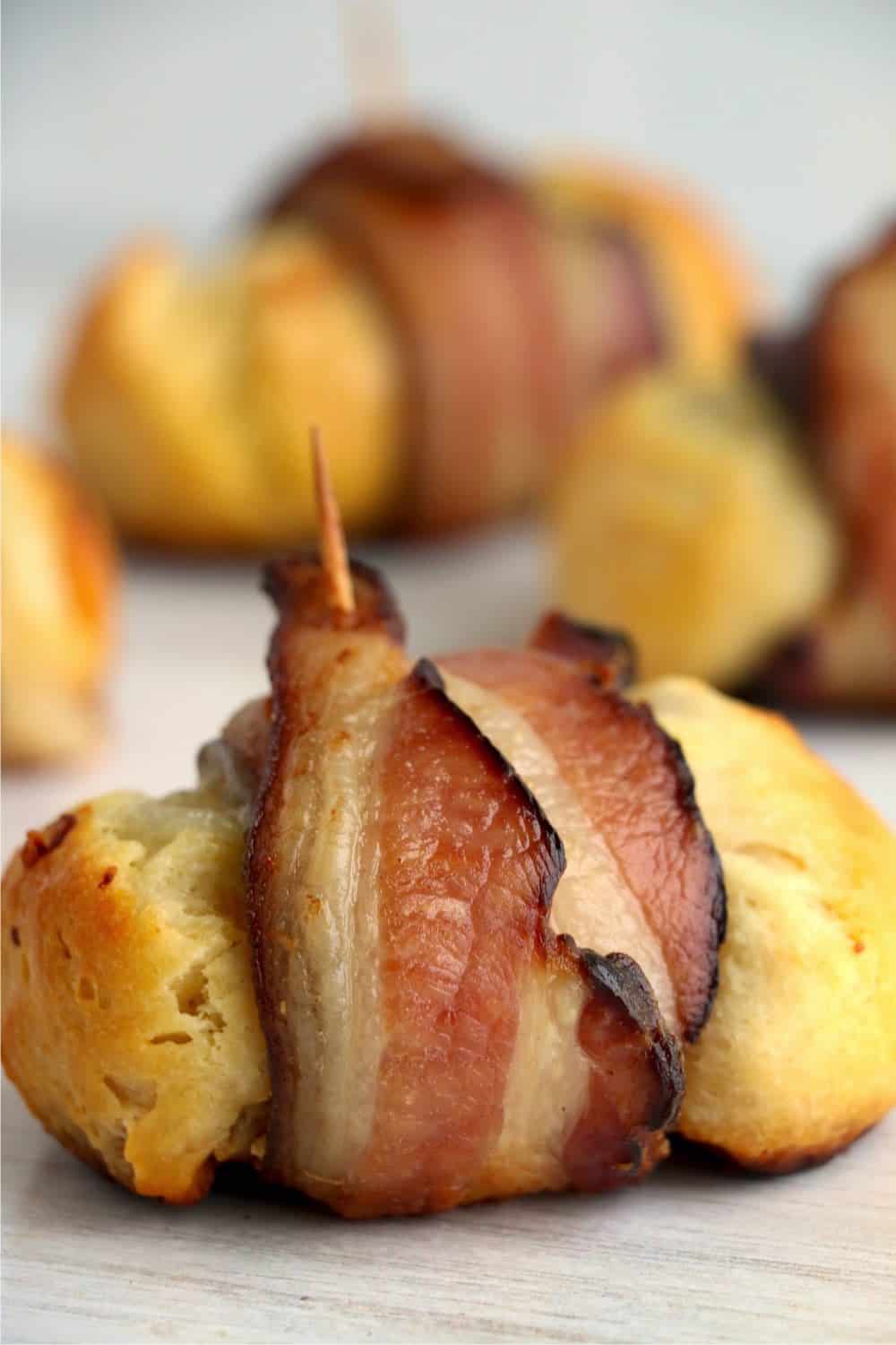 A close-up vertical photograph of a bacon wrapped cheese bomb with a toothpick sticking out the top