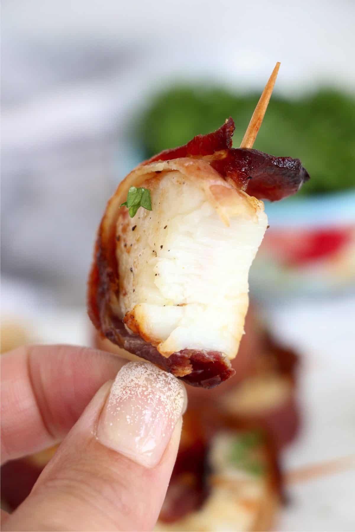 Closeup shot of hand holding an air fryer bacon wrapped scallop on a toothpick