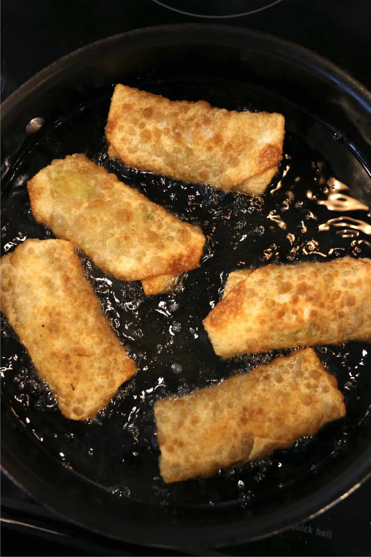 Egg rolls frying in oil in a skillet