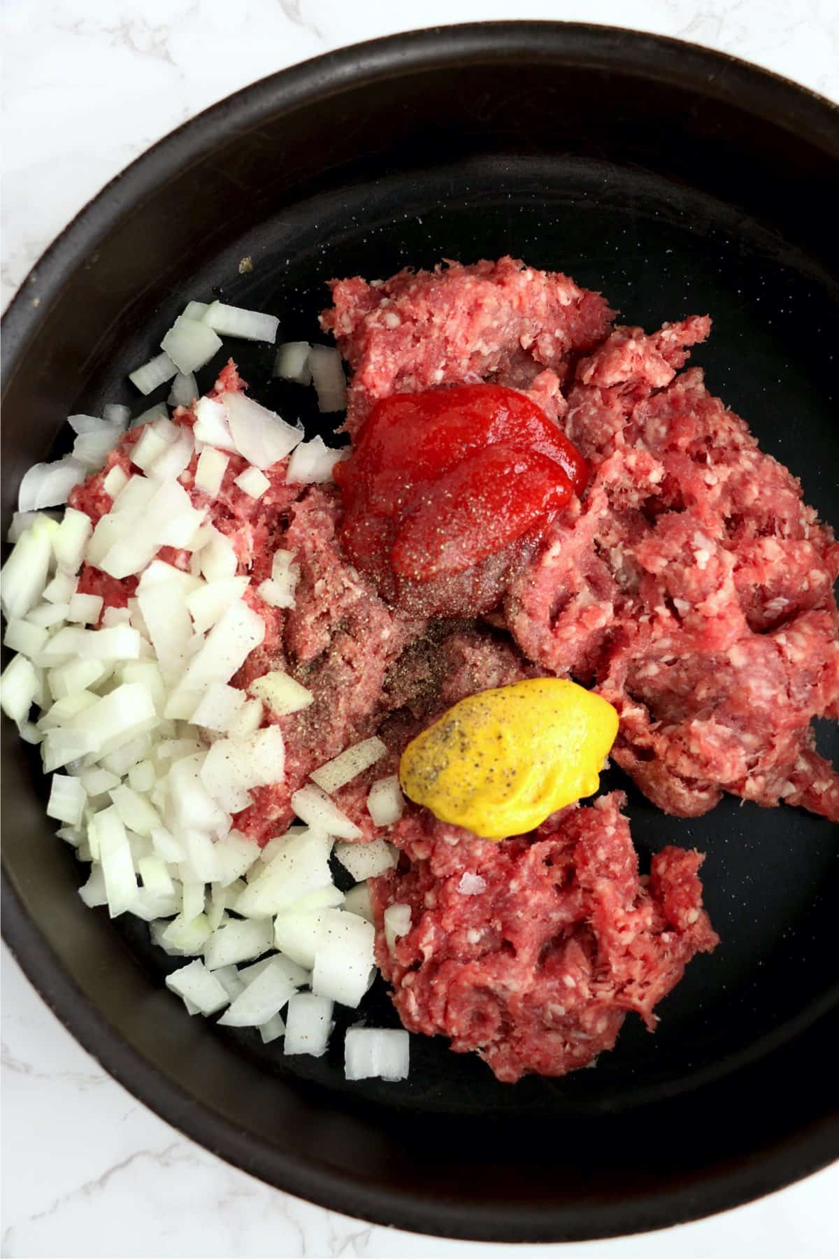 Closeup shot of beef, ketchup, mustard, and onions in skillet