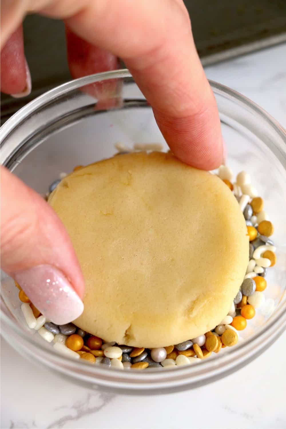 Closeup shot of hand dipping cookie into sprinkles