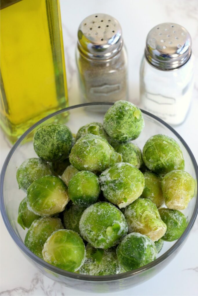 Frozen brussel sprouts in bowl next to salt and pepper shakers