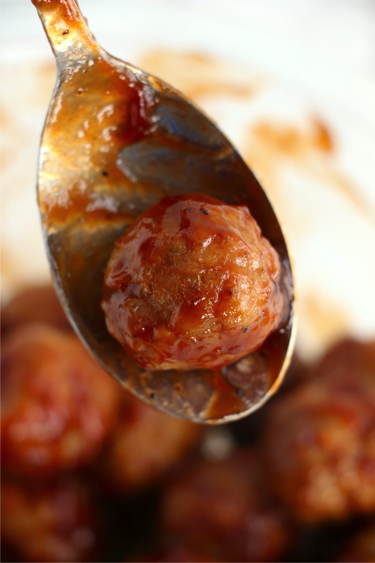 Closeup shot of meatball covered in barbecue sauce on spoon