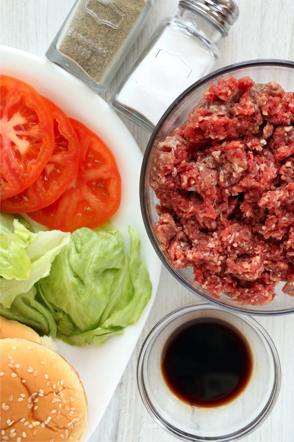 Overhead shot of ground beef in bowl next to buns, lettuce, and tomato on plate