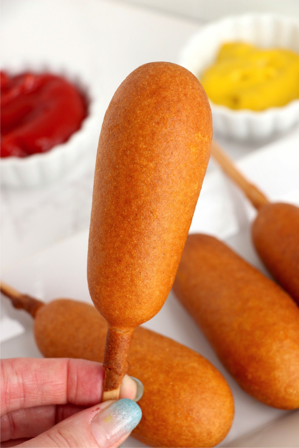Closeup shot of hand holding a corn dog over more air fryer corn dogs on plate