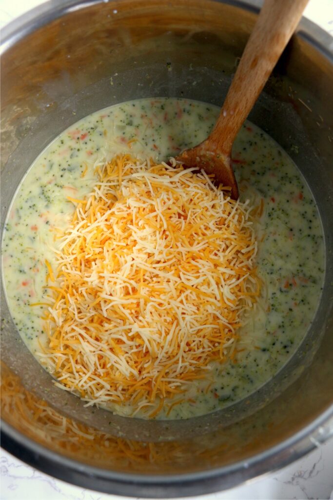 Overhead shot of shredded cheese being stirred into instant pot broccoli cheddar soup