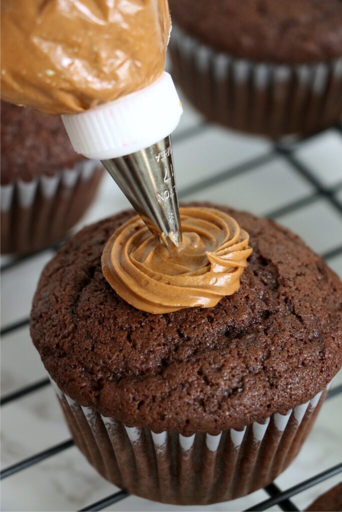  Chocolate cupcake being frosted with brown frosting in the center