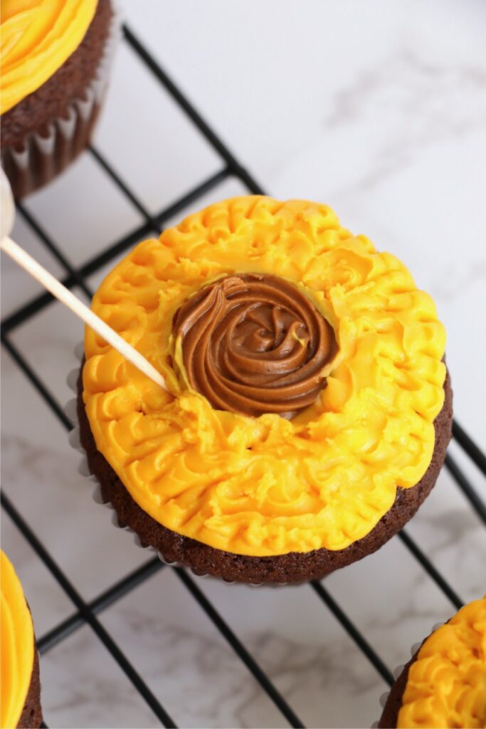 Overhead shot of toothpick being used to texture the frosting on chocolate sunflower cupcake