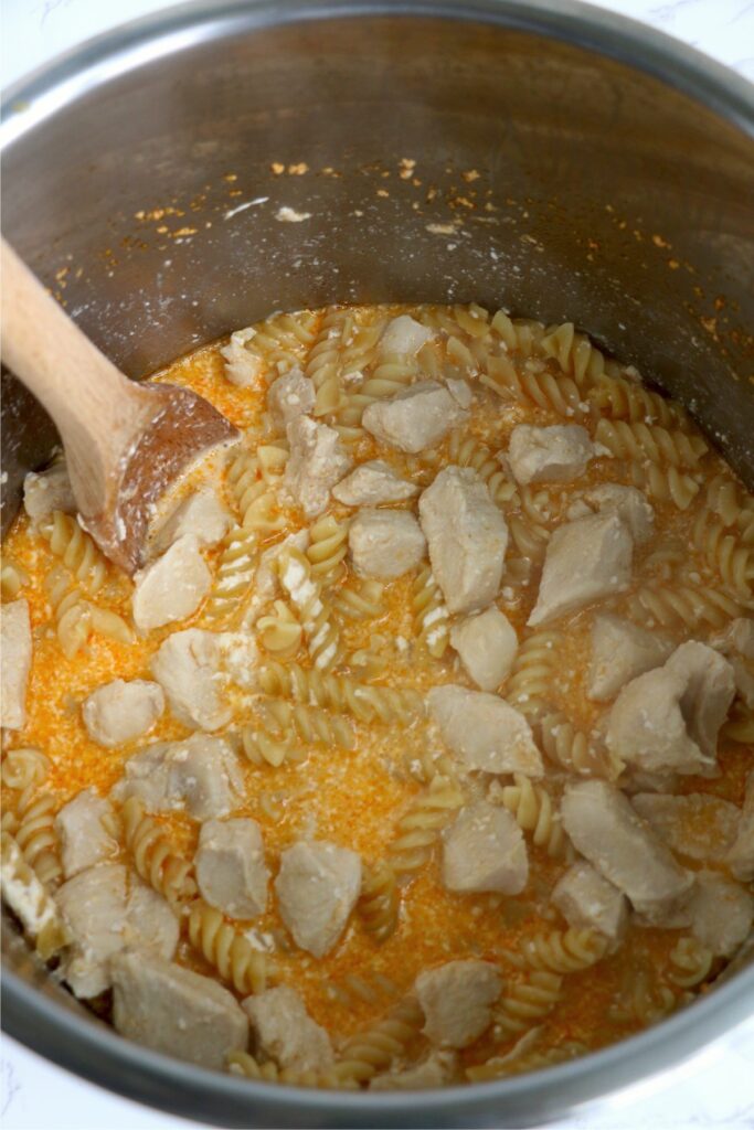 Chicken, pasta, cheese, and sauce being stirred with spoon in instant pot