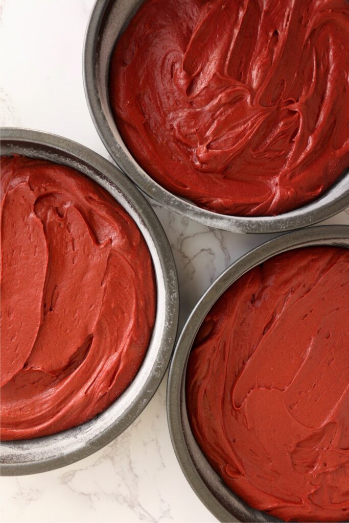 Overhead shot of three round cake pans filled with red velvet cake batter