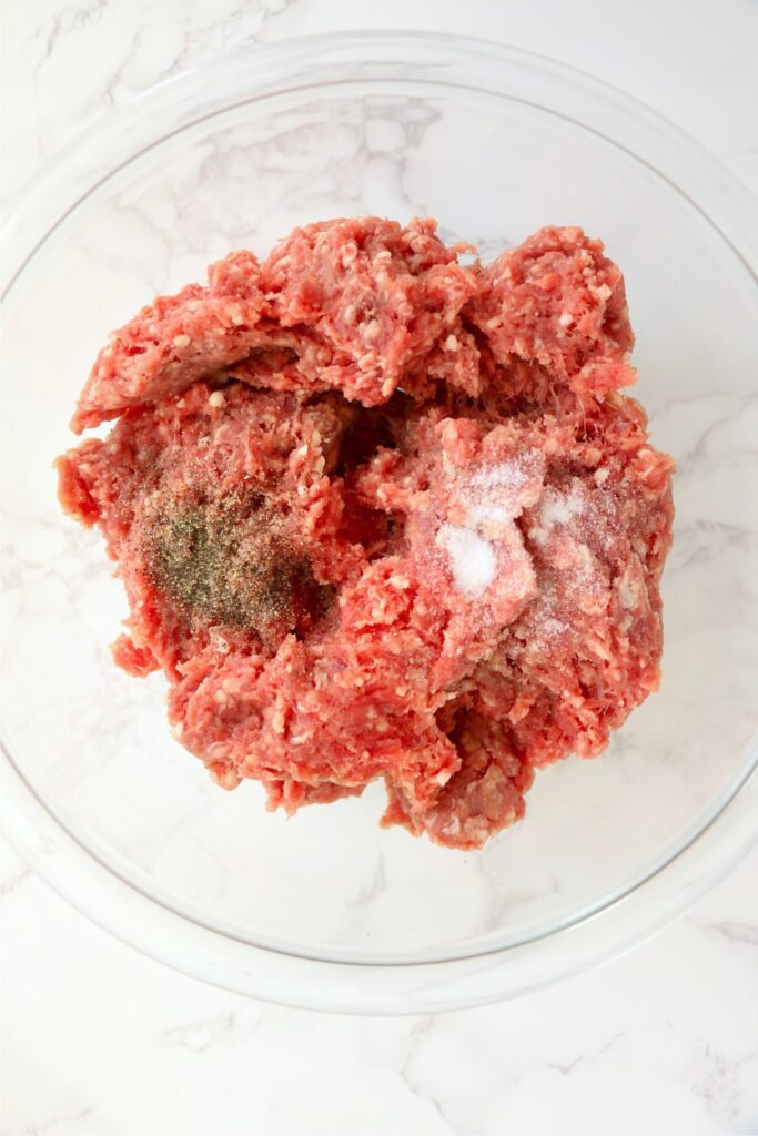 Overhead shot of ground beef, salt, and pepper in bowl.