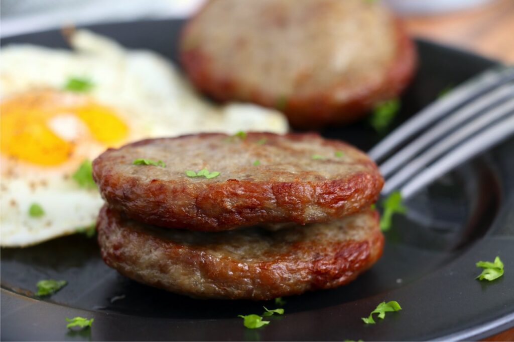 Closeup shot of two air fryer frozen sausage patties on plate with eggs and fork