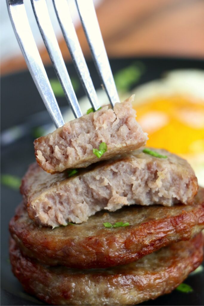 Closeup shot of forkful of sausage pattie on top of air fryer frozen sausage patties stacked atop one another