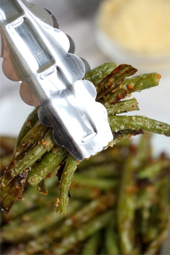 Closeup shot of tongs holding air fryer green beans. 