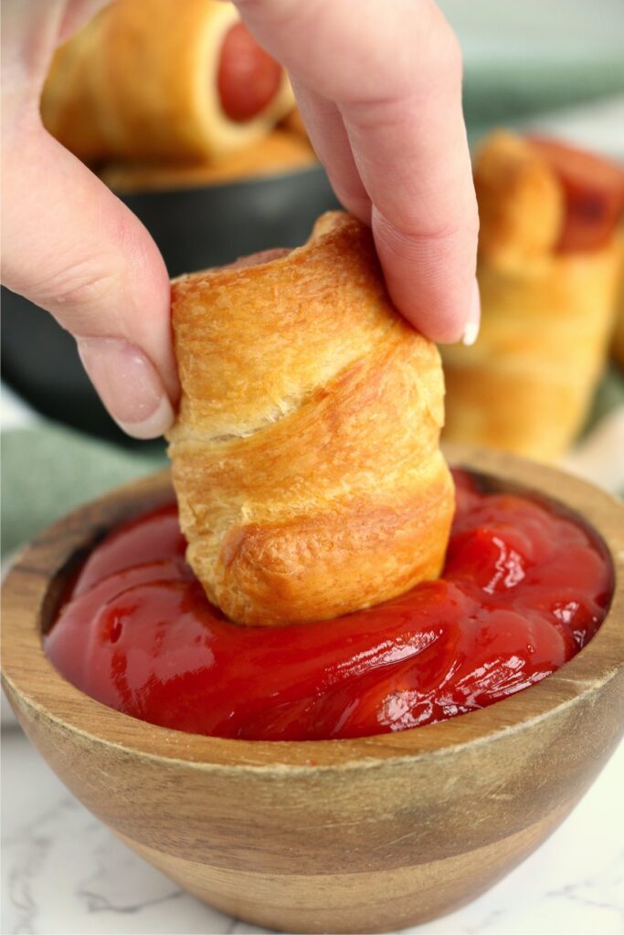 Closeup shot of pig in a blanket being dipped into ketchup.