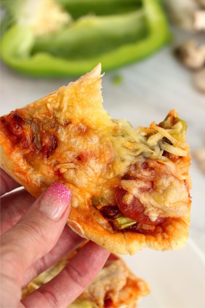 Closeup shot of hand holding an air fryer pizza slice with bite taken out