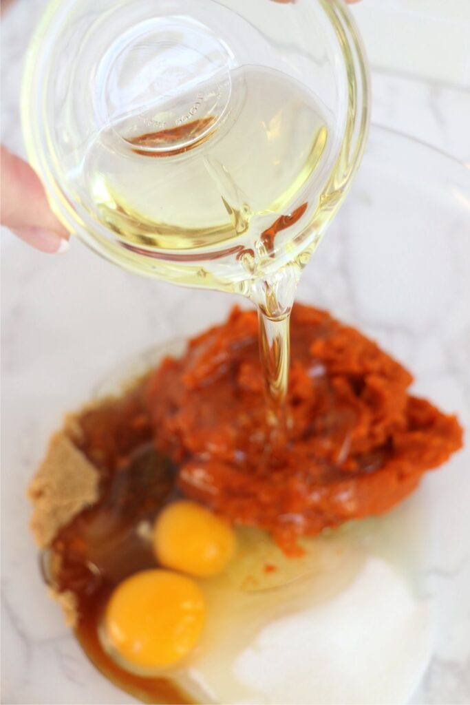 Oil being poured into bowl with pumpkin pie filling, sugar, brown sugar, and eggs in a bowl