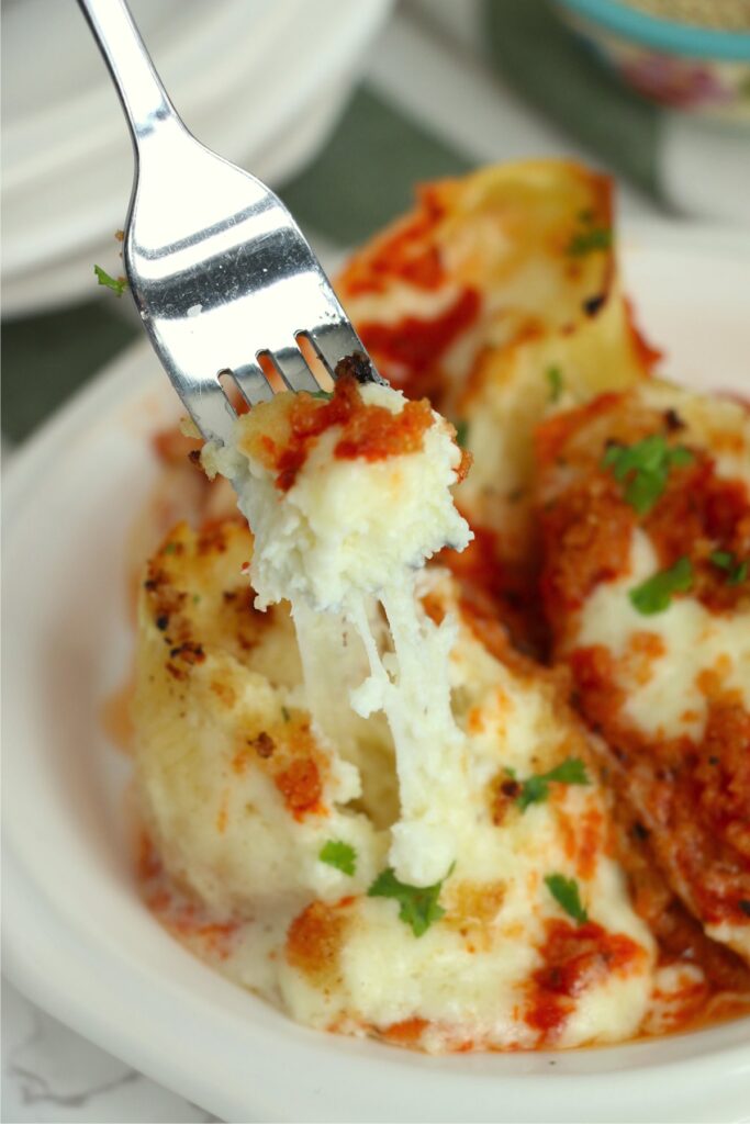 Closeup shot of forkful of sutffed shells over plate of more stuffed shells