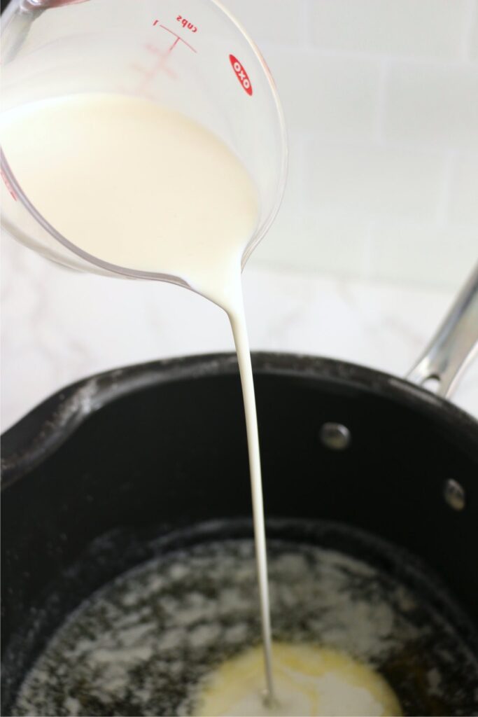 Heavy cream being poured into pot with melted butter