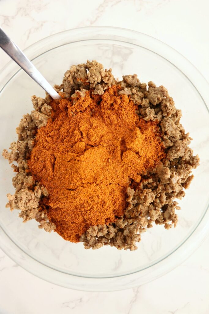 Overhead host of bround beef and taco seasoning in glass bowl