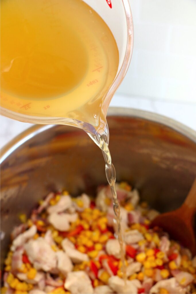 Closeup shot of chicken broth being poured into instant pot with chicken and vegetables