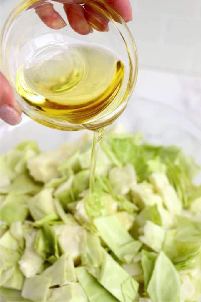 Olive oil being poured from a small bowl over a bowl of cabbage