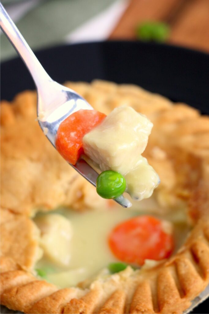 Closeup shot of forkful of chicken and vegetables over a chicken pot pie