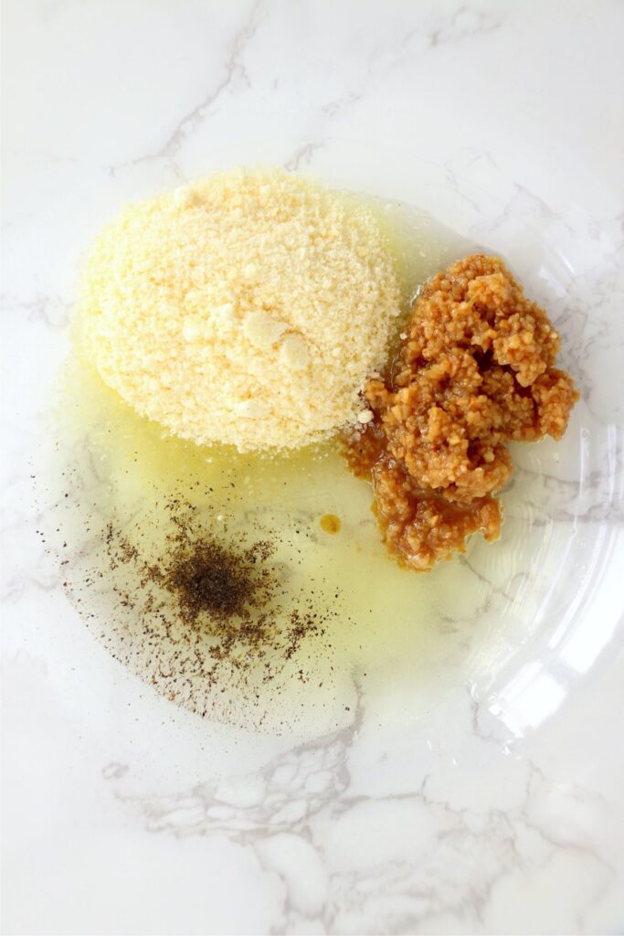 Closeup overhead shot of garlic, parmesan cheese, pepper, and oil in bowl