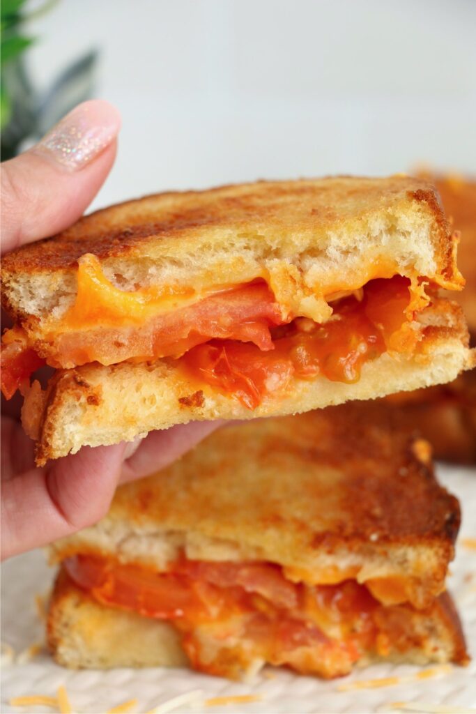 Closeup shot of hand holding half of an air fryer grilled cheese and tomato sandwich