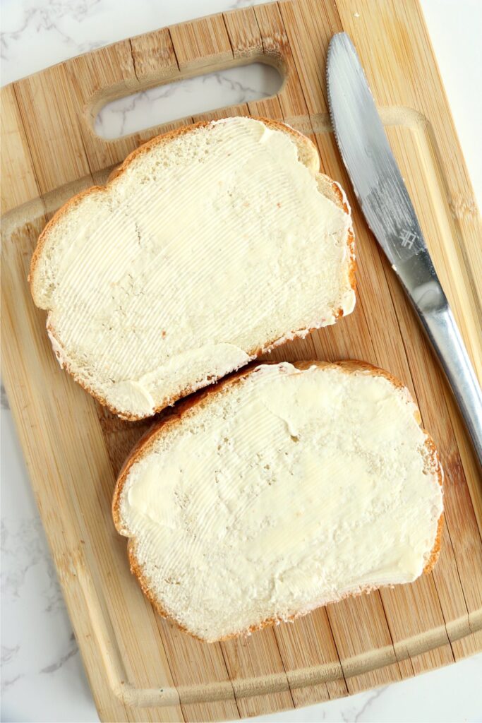 Overhead shot of buttered bread next to butter knife on cutting board