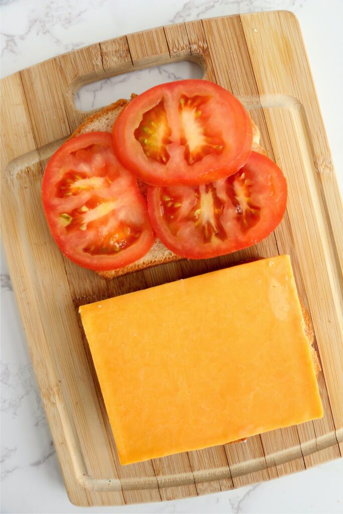 Overhead shot of tomato slices on a piece of bread next to a piece of bread with cheese on it