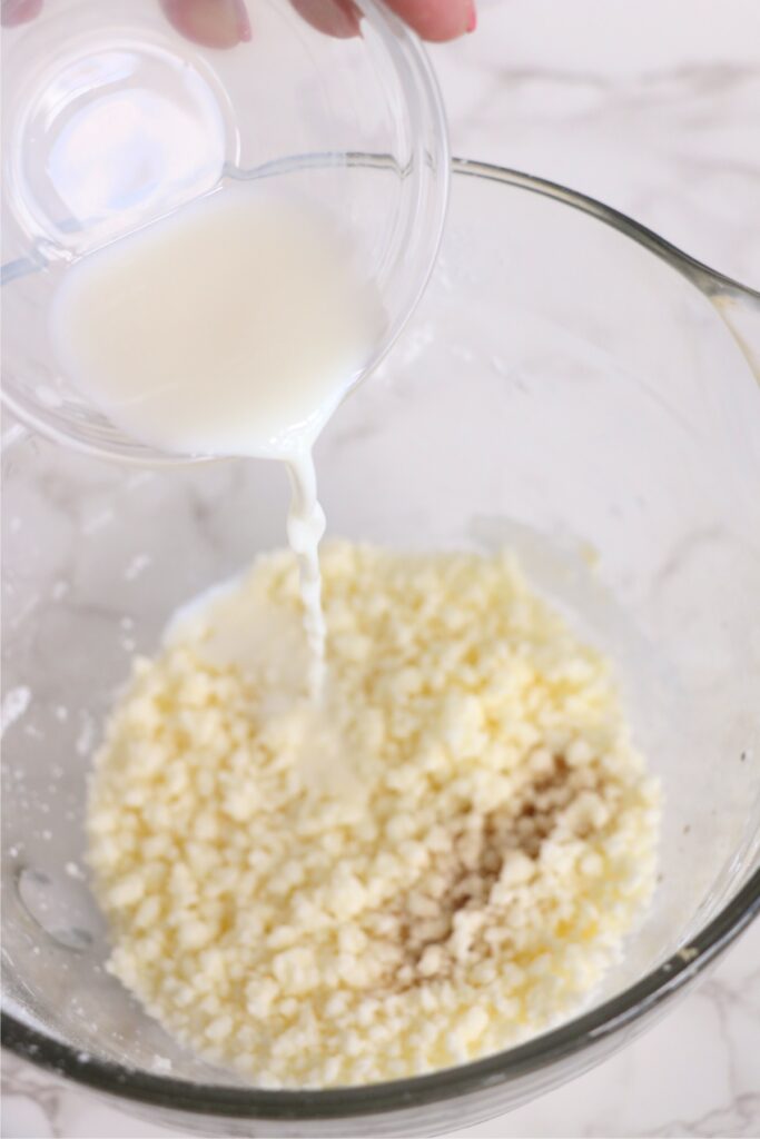 Milk being poured into powdered sugar in mixing bowl