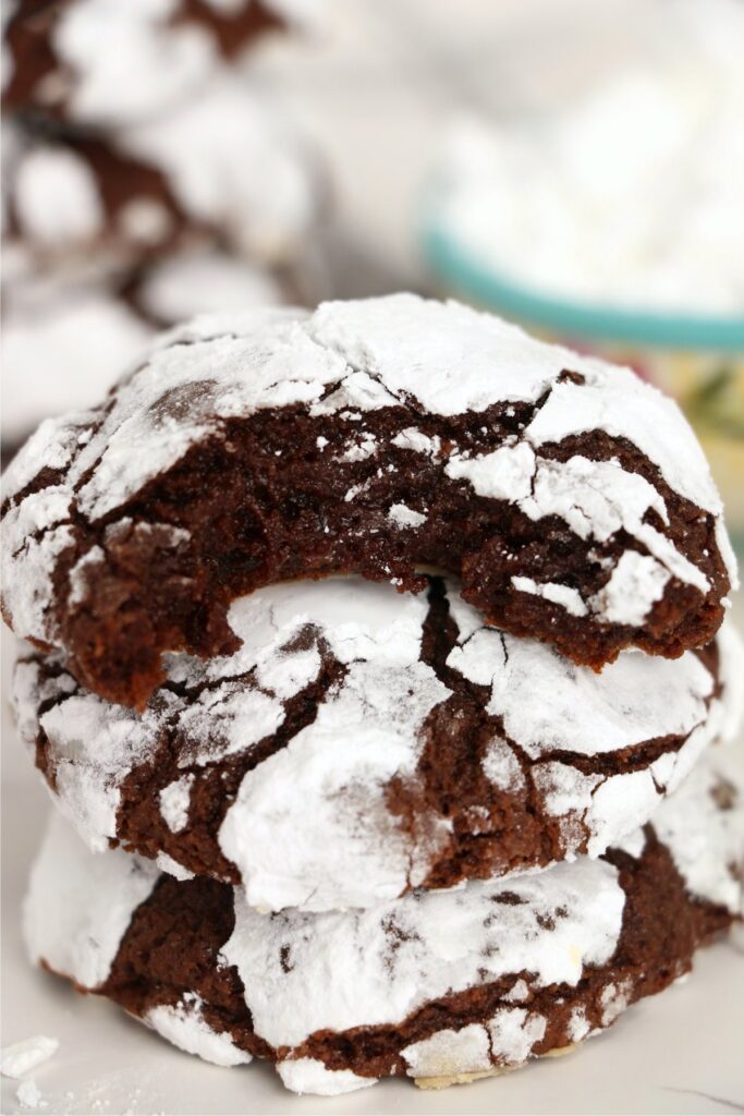 Closeup shot of chocolate crack cookies stacked atop one another with bite taken out of top cookie.