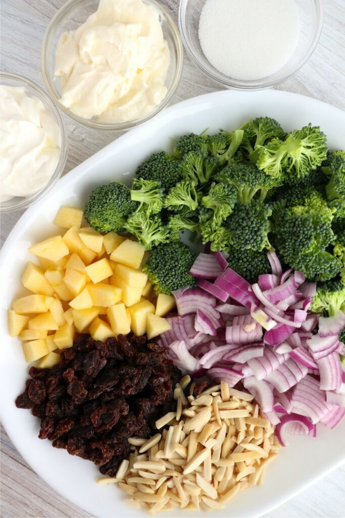 Overhead shot of broccolie, apples, raisings, nuts, and onions on plate