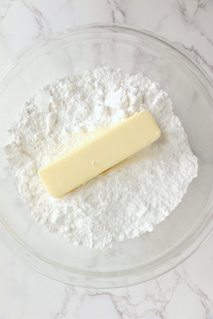 Overhead shot of stick of butter on top of powdered sugar in bowl